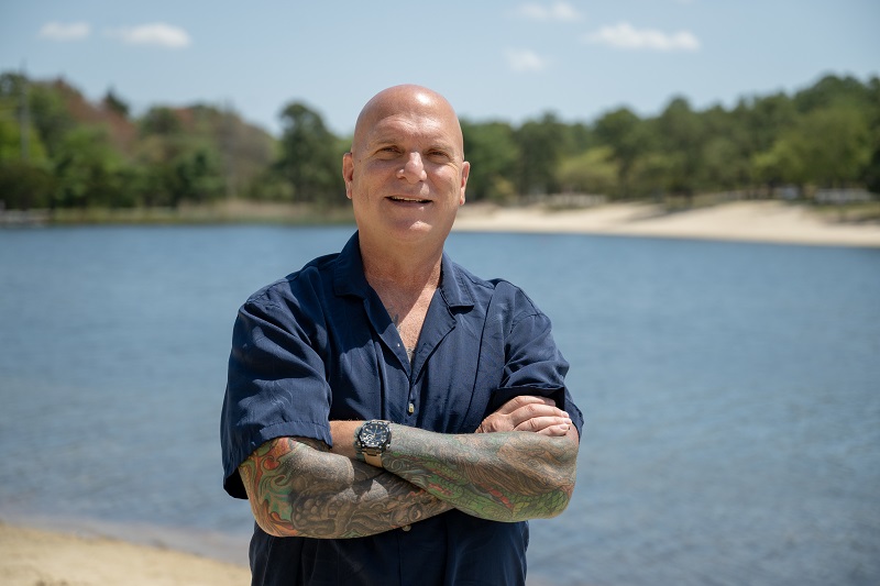 Leonard DiMatteo standing, smiling with his arms crossed, in front of a body of water.