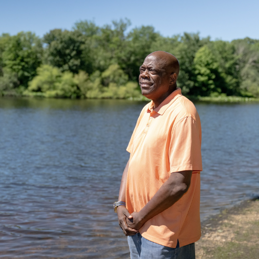 Standing near a scenic body of water, heart transplant recipient Joe Johnson gazes into the distance.