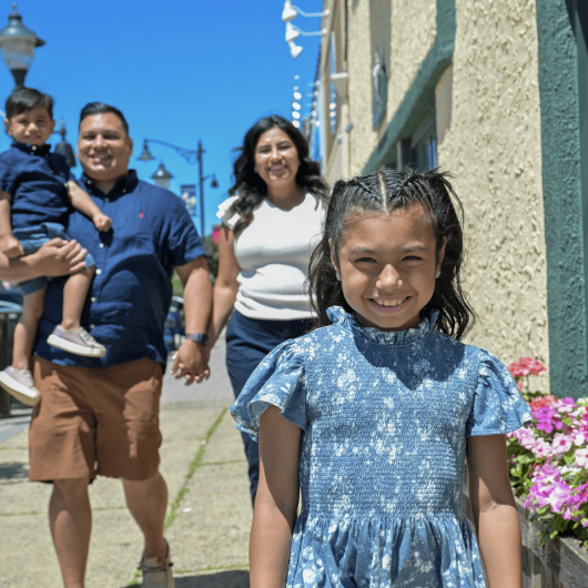 A little girl who received a kidney transplant smiles at the camera as her mom, dad and little brother look on.