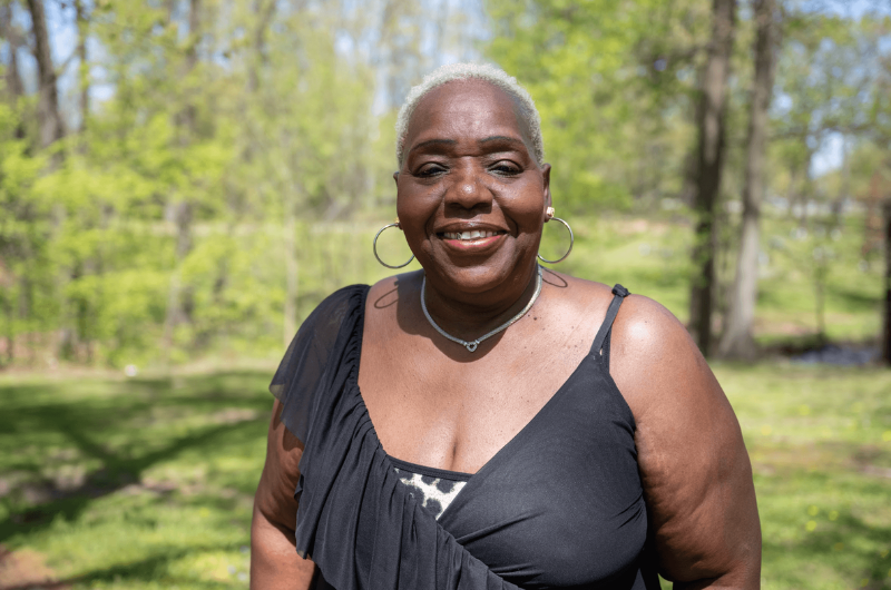 Fosteen Brathwaite, 69, of Avenel, New Jersey, smiles at the camera with greenery behind her.