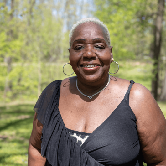Fosteen Brathwaite, 69, of Avenel, New Jersey, smiles at the camera with greenery behind her.