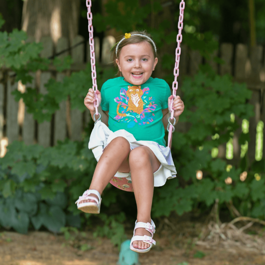 A little girl laughs and smiles at the camera while swinging on a swing