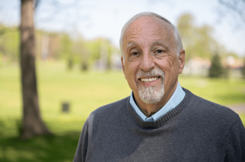 68-year-old Lenny Croog smiles at the camera with greenery behind him.