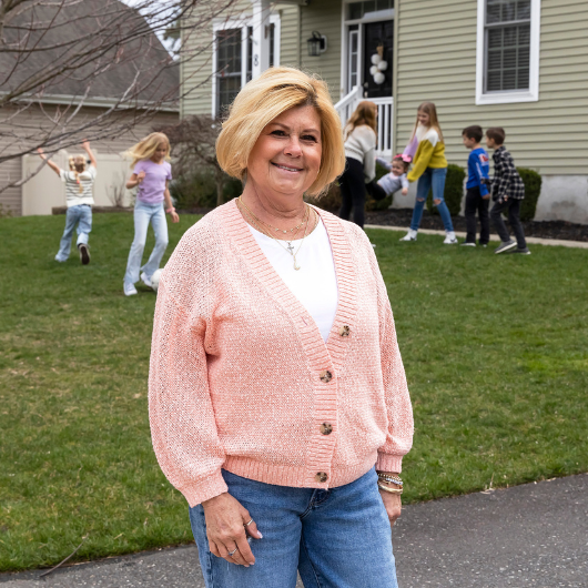 Geralyn Fogarty, now 67, stands in her front yard as her grandchildren play in the background.