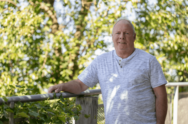 John Drexler leans up against a fence and smiles at the camera.