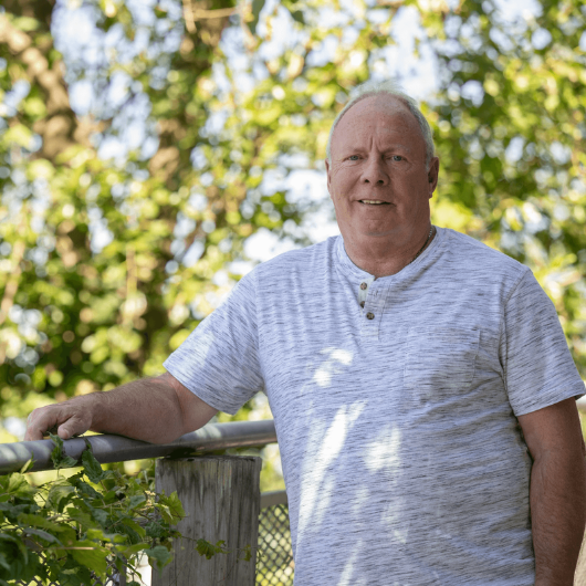 John Drexler leans up against a fence and smiles at the camera.
