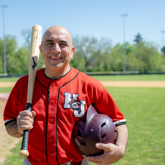 James Morales stands on a baseball field holding a baseball bat and helmet.