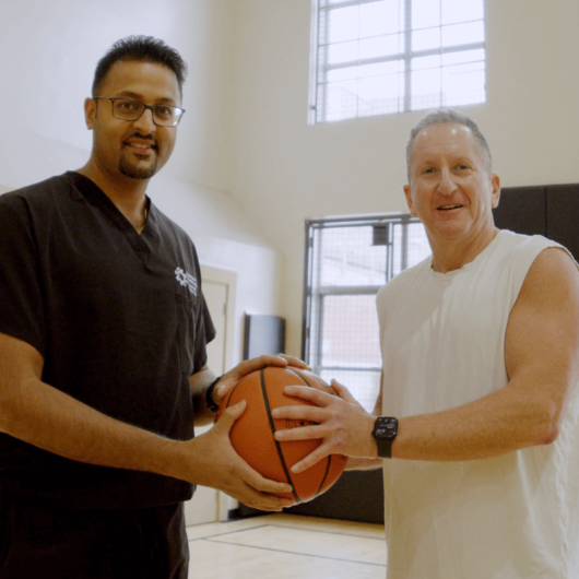 63-year-old Robert Cohan holds a basketball next to orthopedic surgeon Siddhant Mehta, M.D., Ph.D.