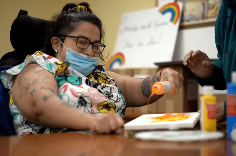 Isabell Villacis, who has cerebral palsy, sits at a craft table and pours out some paint.