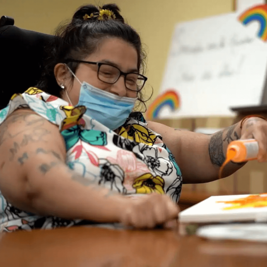 Isabell Villacis, who has cerebral palsy, sits at a craft table and pours out some paint.