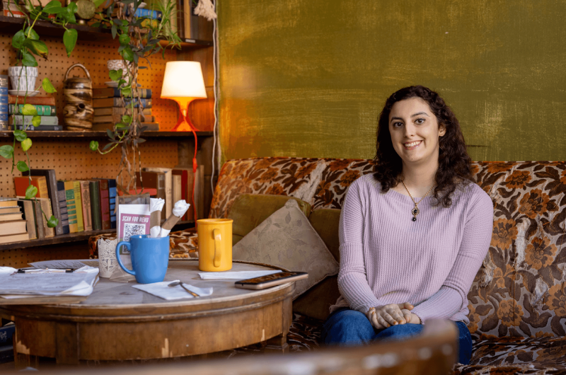 Melanie Ferraz sits on a floral sofa and smiles.