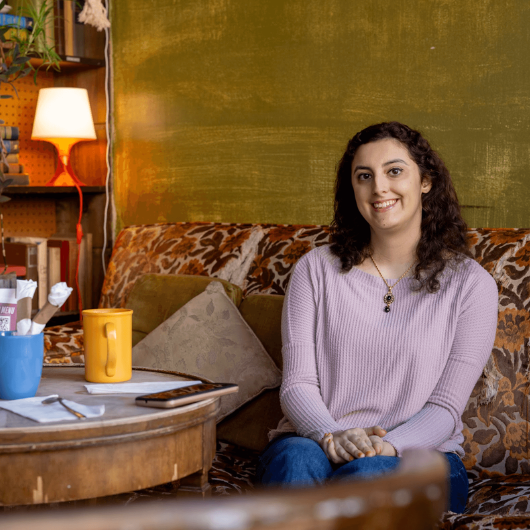 Melanie Ferraz sits on a floral sofa and smiles.