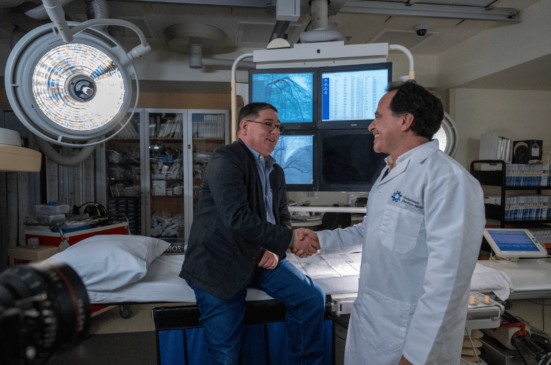 While sitting on an exam table, Charlie Cocuzza shakes hands with cardiologist Shaddy Younan, M.D.