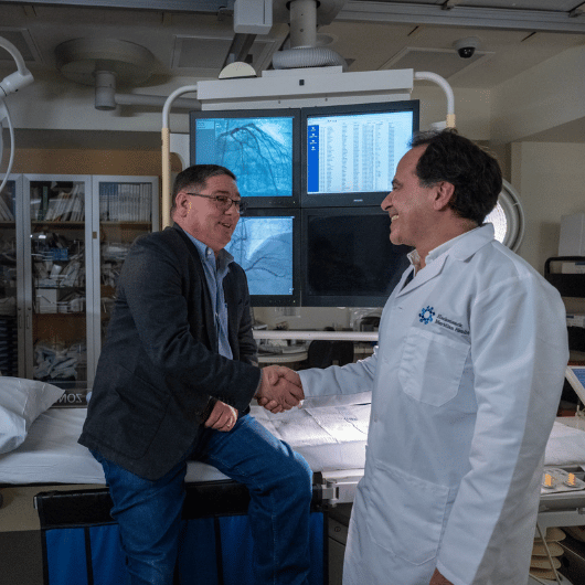 While sitting on an exam table, Charlie Cocuzza shakes hands with cardiologist Shaddy Younan, M.D.