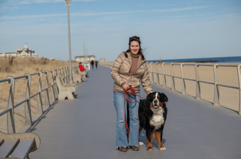 Standing on a beach boardwalk, Kathy Bierker and her dog look at the camera.