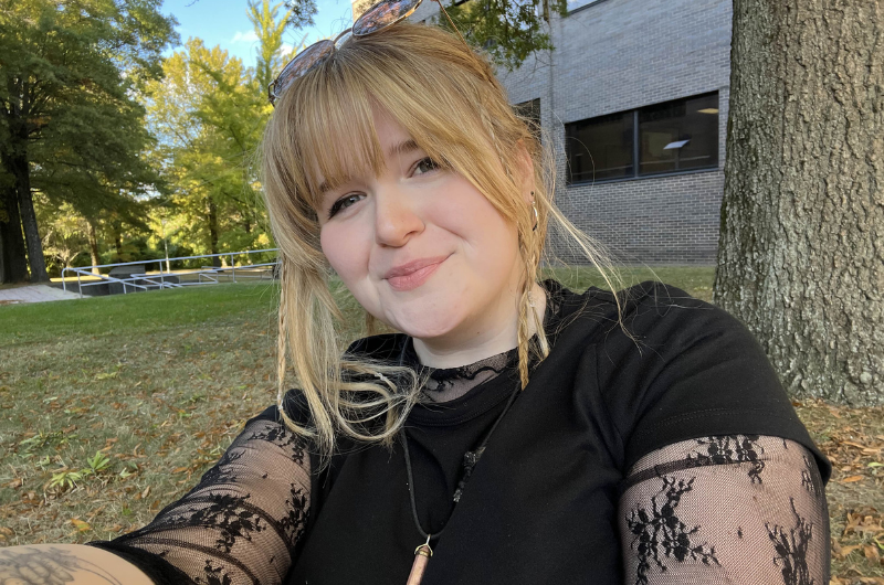 College student sits by a tree.