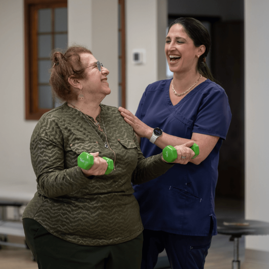 Mary Ann Brancato holds dumbbells and smiles at her therapist.   