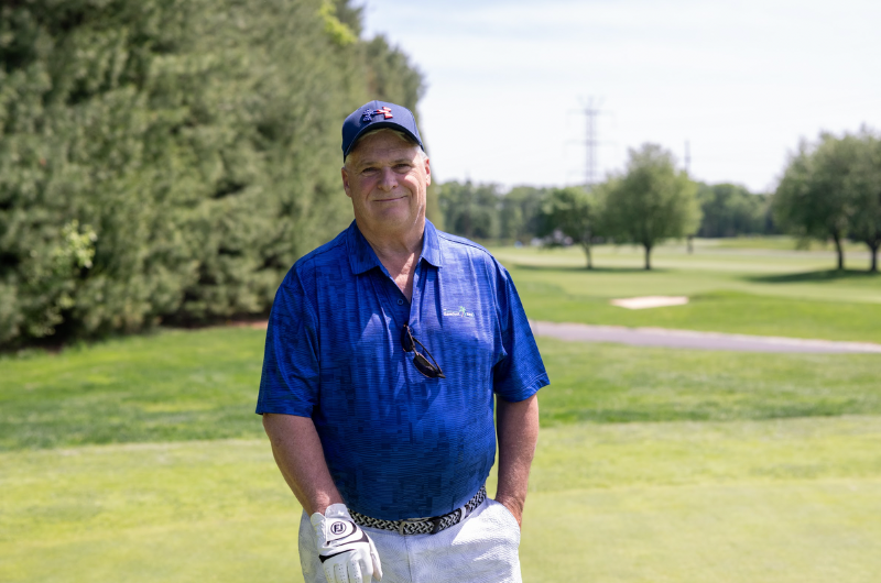 68-year-old Jimmy Colby stands on a golf course and smiles.