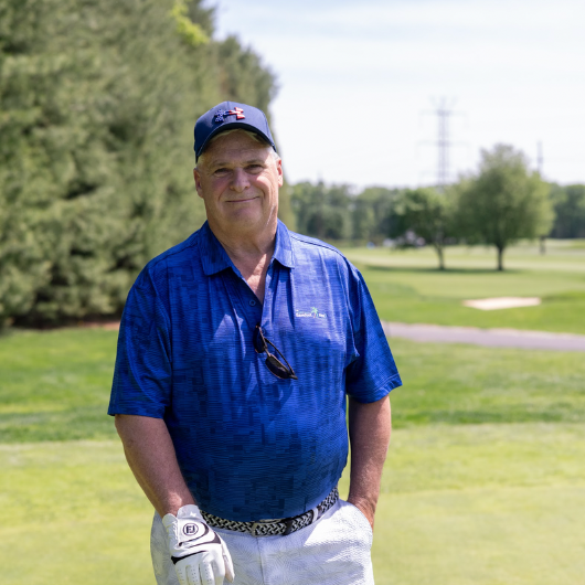 68-year-old Jimmy Colby stands on a golf course and smiles.