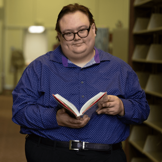 36-year-old Gary Galgoci holds an open book and smiles at the camera.