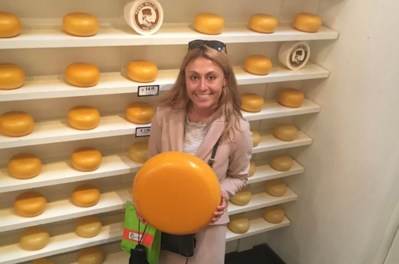 31-year-old Cara Morelli, from Manalapan, NJ, holds a wheel of cheese and smiles at the camera.
