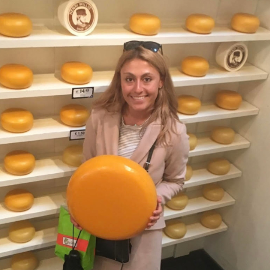 31-year-old Cara Morelli, from Manalapan, NJ, holds a wheel of cheese and smiles at the camera.