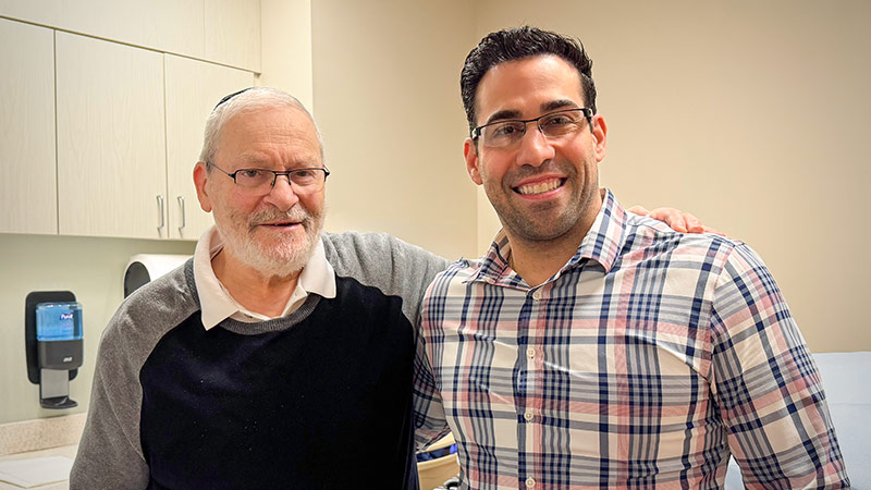 Elazer Lew stands in an exam room and smiles at the camera.