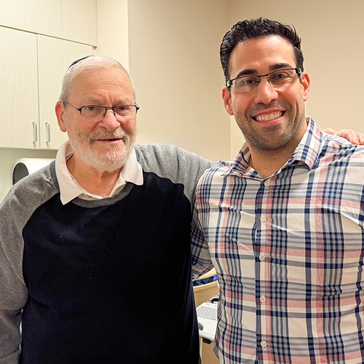 Elazer Lew stands in an exam room and smiles at the camera.