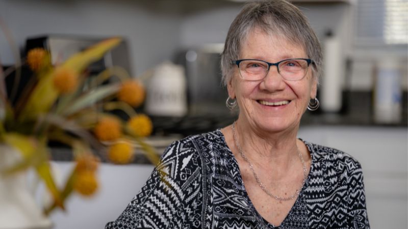 74-year-old Cecelia Lucas sits with a cup of coffee and smiles at the camera.