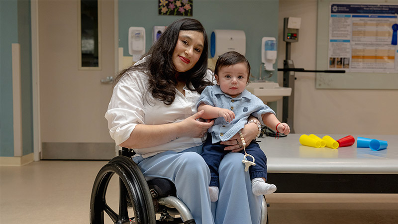 While sitting in a wheelchair, Jessica Espinoz holds her son in her lap.