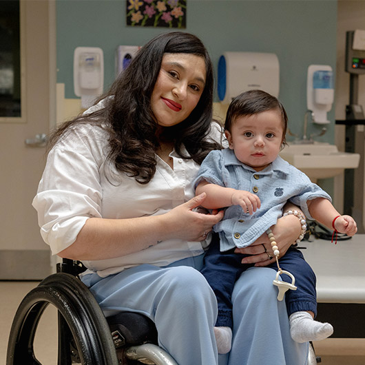 While sitting in a wheelchair, Jessica Espinoz holds her son in her lap.