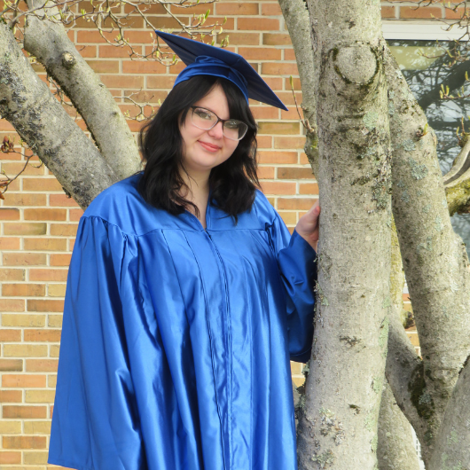 Wearing a blue graduation cap and gown, Skylyn smiles at the camera. 