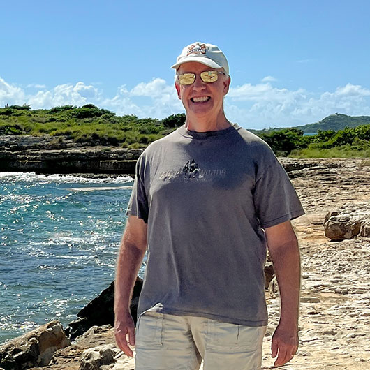 Eric Lewanda smiles in front of a turquoise ocean background.