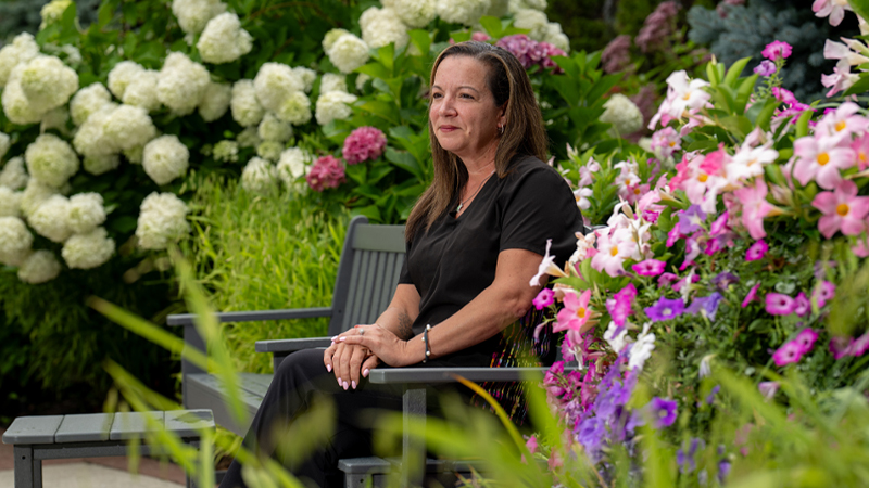 Maureen D. sits on a park bench looking off into the distance.