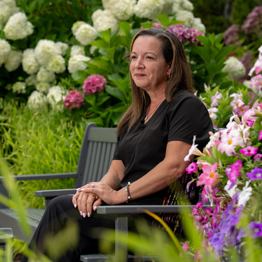 Maureen D. sits on a park bench looking off into the distance.