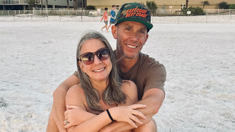 Colleen and Bryan Schultz sit on a sandy beach together.