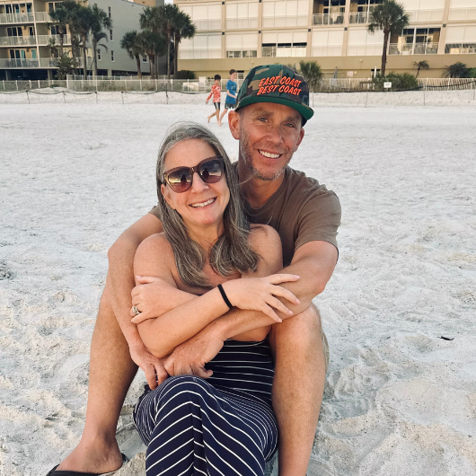 Colleen and Bryan Schultz sit on a sandy beach together.
