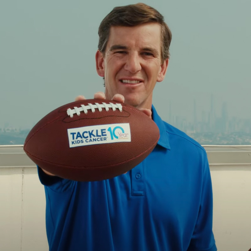 Eli Manning Holding a Football for Tackle 10 Kids Cancer Program