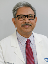 Man with grey hair, glasses, moustache wearing a white coat and red tie