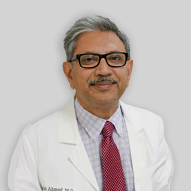 Man with grey hair, glasses, moustache wearing a white coat and red tie
