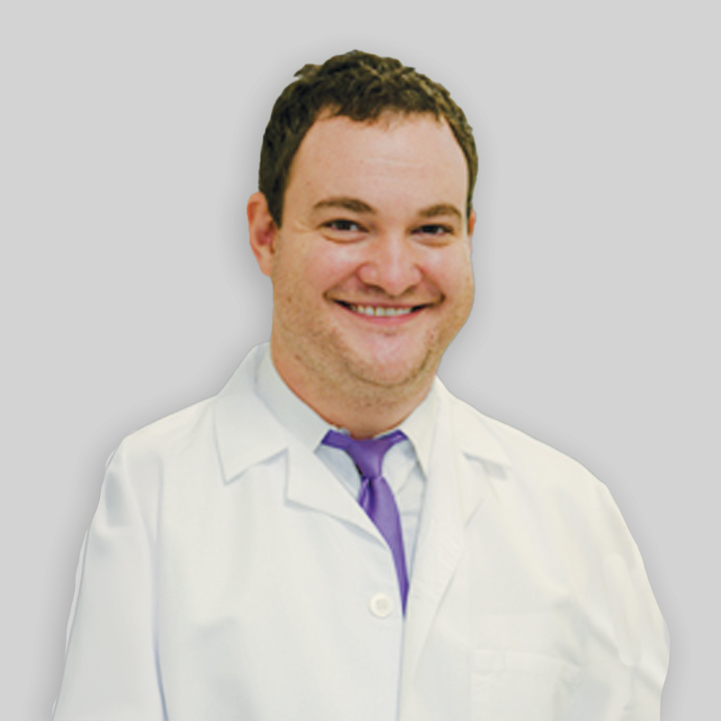 Man with short brown hair smiling while wearing a white lab coat