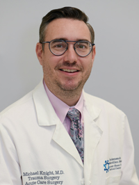 Man with glasses and short brown hair smiling while wearing a lab coat