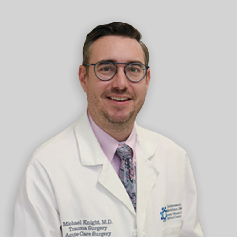 Man with glasses and short brown hair smiling while wearing a lab coat