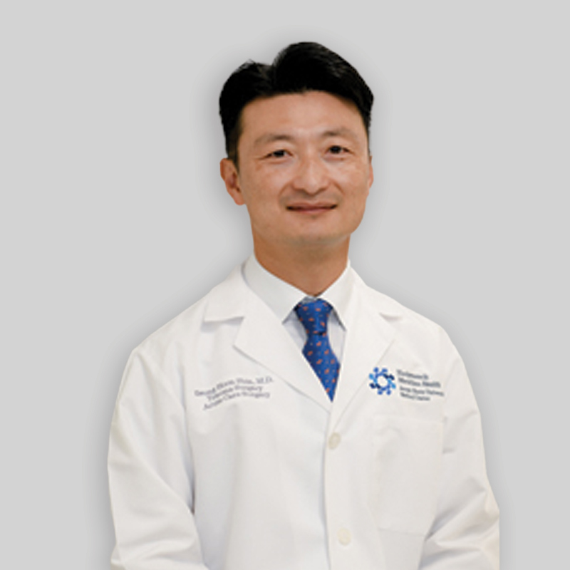 Man with short wavy black hair wearing a blue tie in a white lab coat