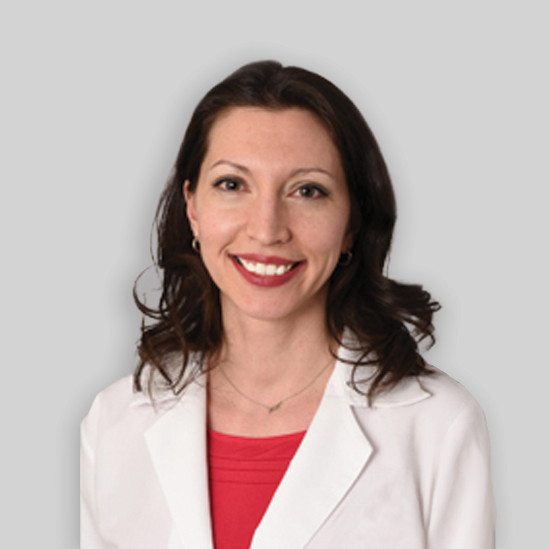 Women wearing red shirt and white lab coat with long brown hair smiling