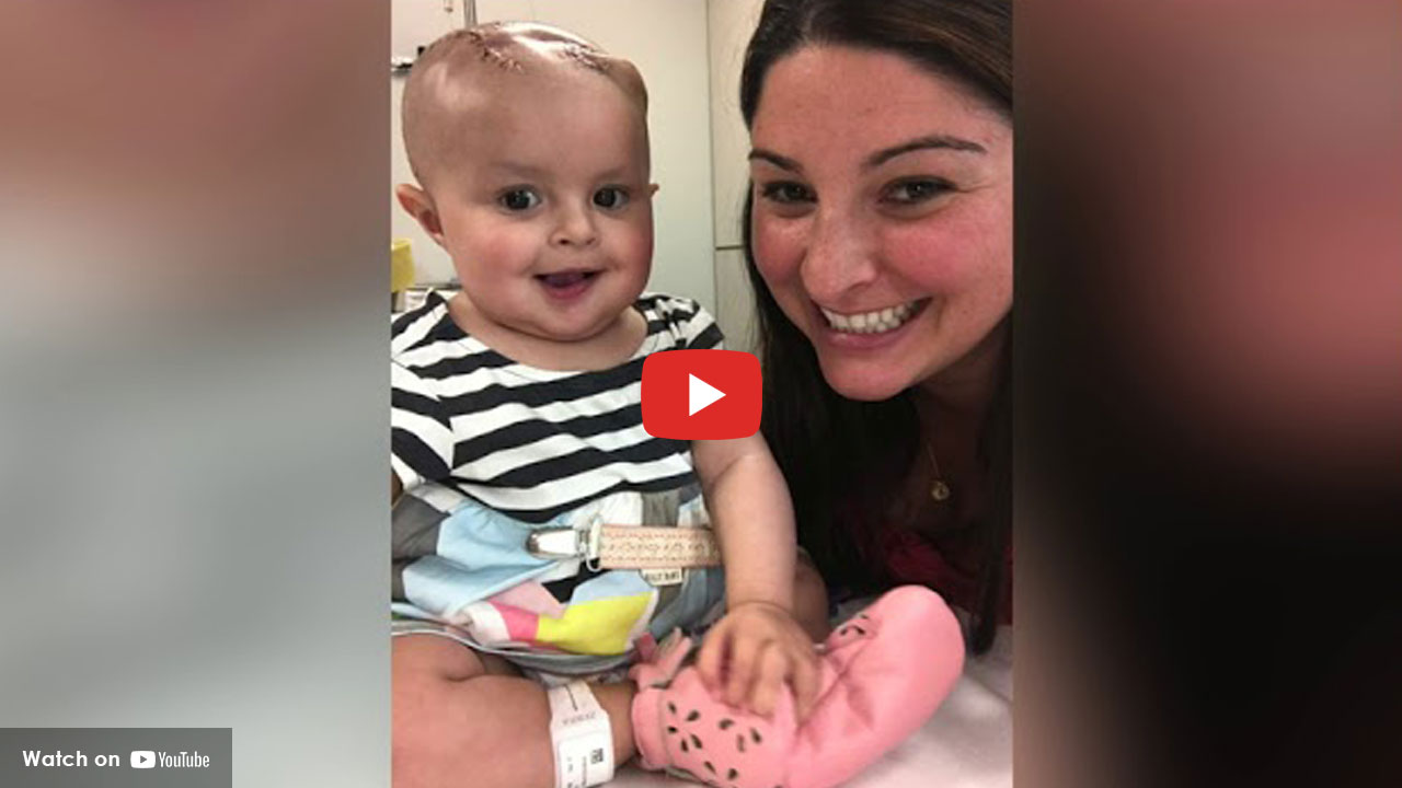 Smiling infant with healing head incision beside caregiver in hospital room