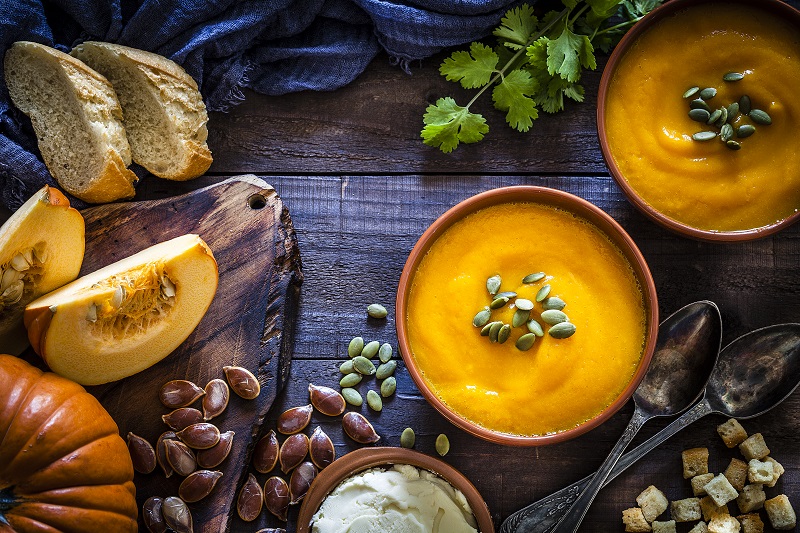 Assortment of pumpkin foods on a table - pumpkin soup, pumpkin seeds, and cut pumpkin.