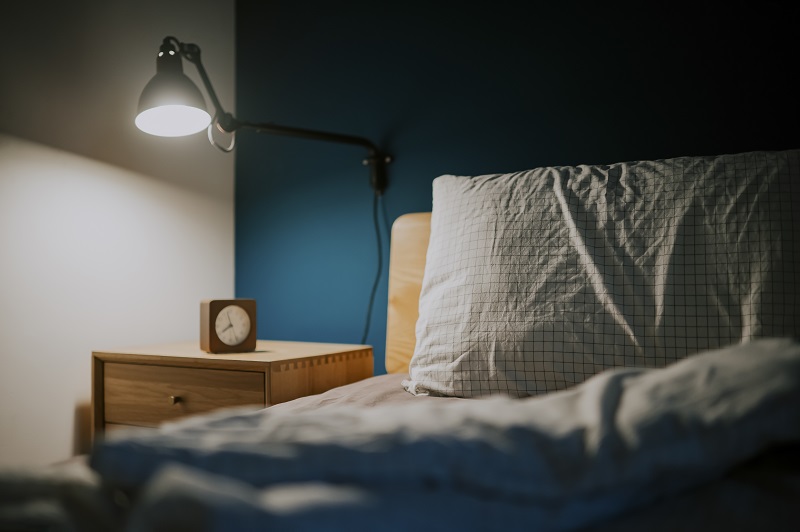 bedroom at night illuminated by electric lamp with clock on night table beside the bed with blue wall