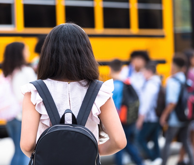 A female middle school student walks hesitantly to the school bus on the first day of school.