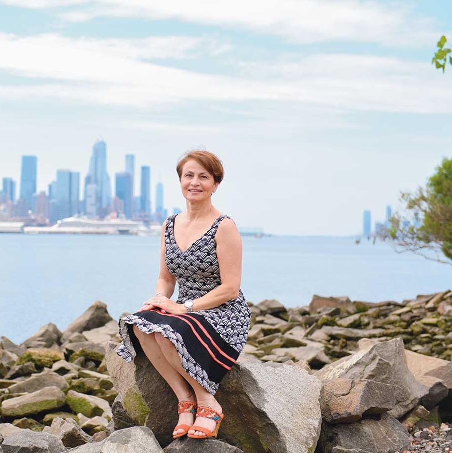 Woman in dress sitting on rocks across from city skyline